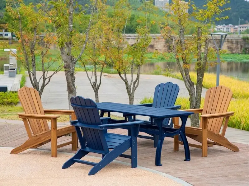 Navy blue and teak HDPE Adirondack chairs with matching dining table set in a riverside public park